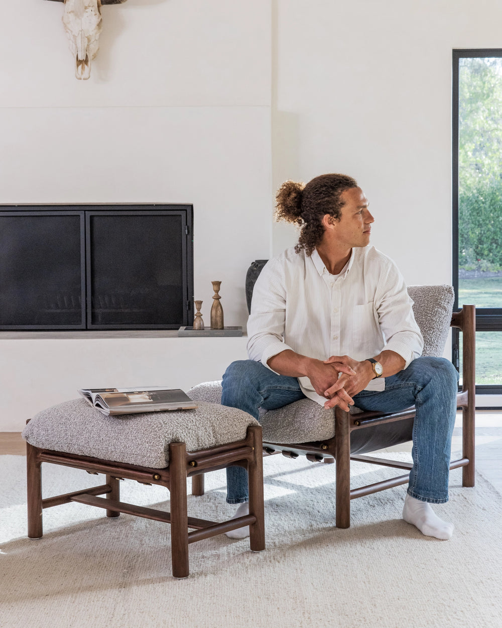 A tranquil living room setting with a man sitting comfortably between two Avon Lounge pieces with textured light grey cushions and elegant dark wooden frames.